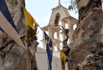a distant cross is seen with a foreground of flags